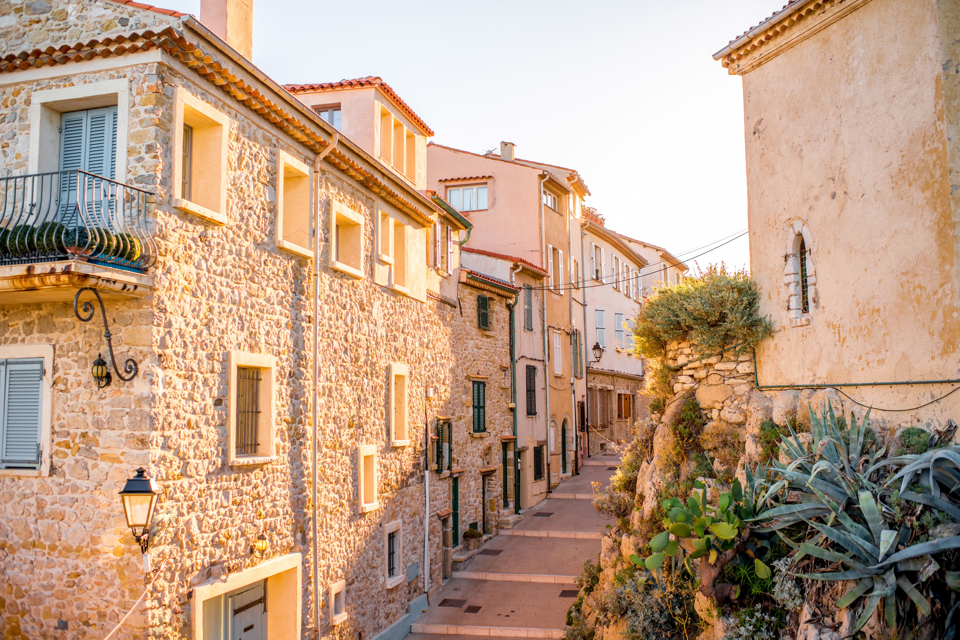 Imagem com ruas da cidade de Antibes em um convidativo e pitoresco cenário com casinhas seculares em tons pastel que contrastam com o azul do céu. 