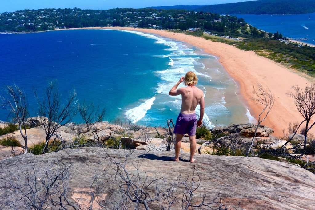 Homem de costas sobre uma pedra com vista para as praias de Palm Beach, em Sydney, na Austrália