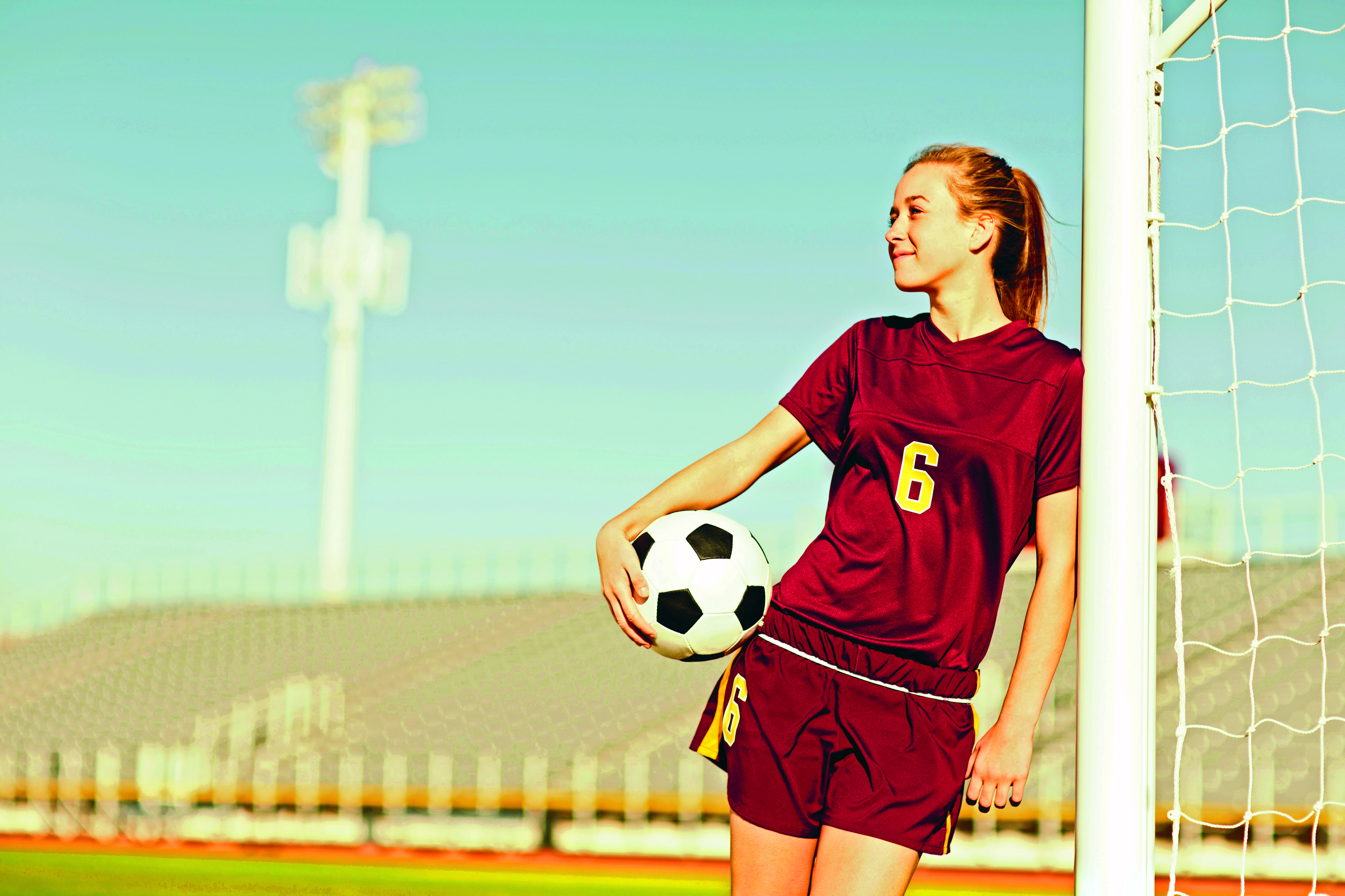 Menina uniformizada segura bola de futebol em campo de escola americana